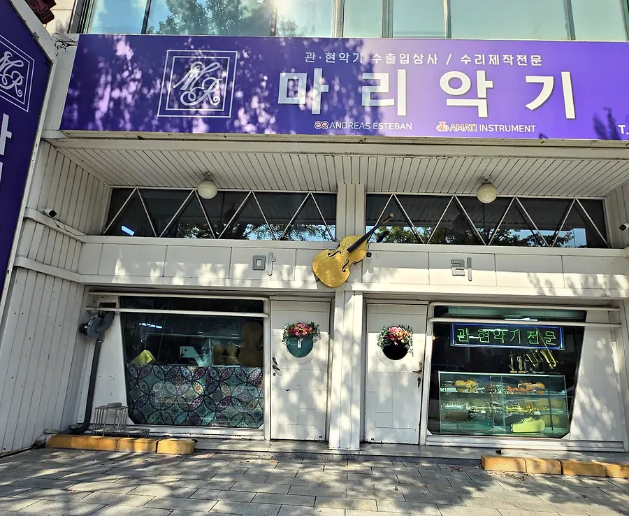 보라색 간판과 금색 첼로 조형물이 있는 매장 외관